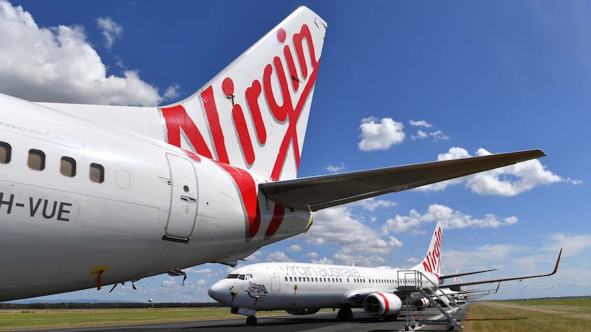 The tail of a Virgin Australia plane on the tarmac, with other planes lines up behind it.
