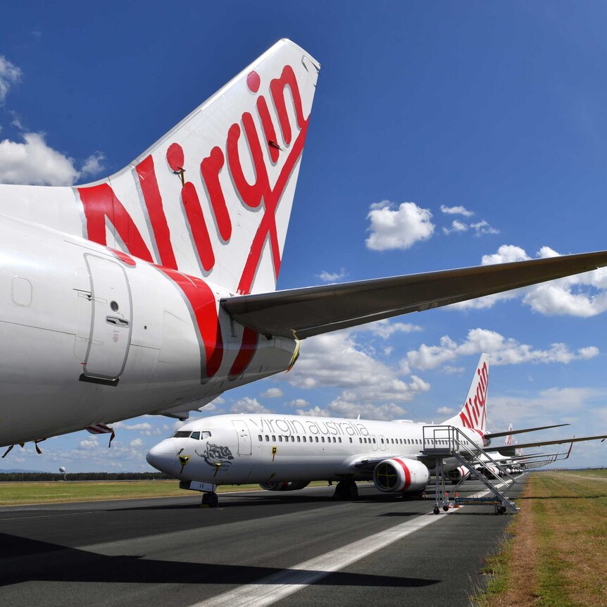 The tail of a Virgin Australia plane on the tarmac, with other planes lines up behind it.