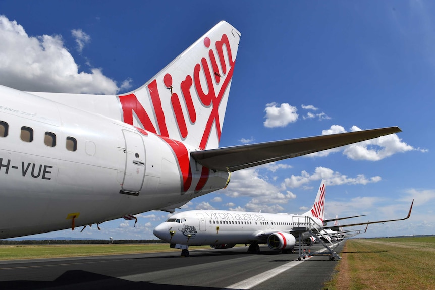 The tail of a Virgin Australia plane on the tarmac, with other planes lines up behind it.