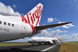 The tail of a Virgin Australia plane on the tarmac, with other planes lines up behind it.