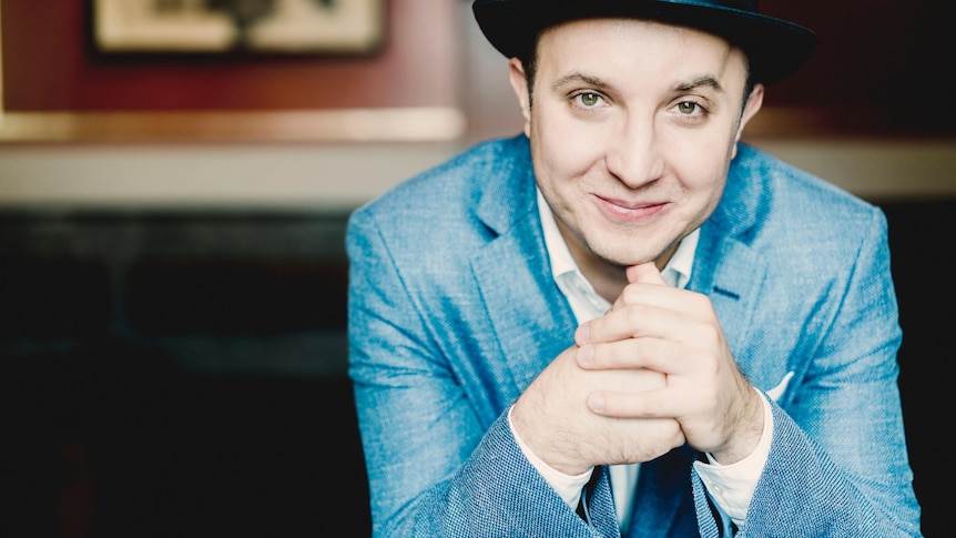 Pianist Alexander Gavrylyuk smiling in a blue jacket and black hat.