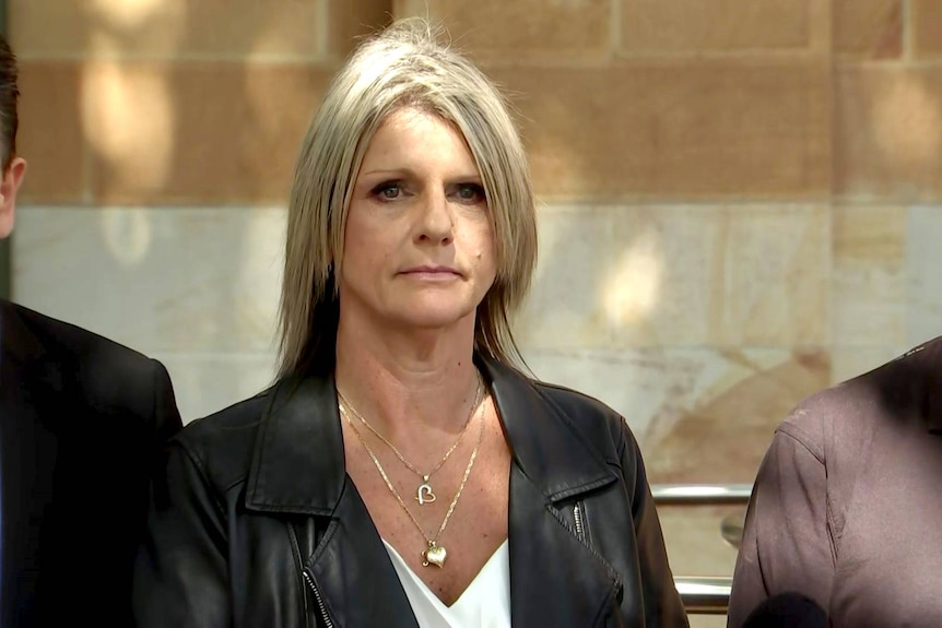 A woman flanked by two other people at a media conference.