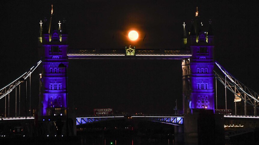 Bright orange full moon behind ornate bridge with two towers