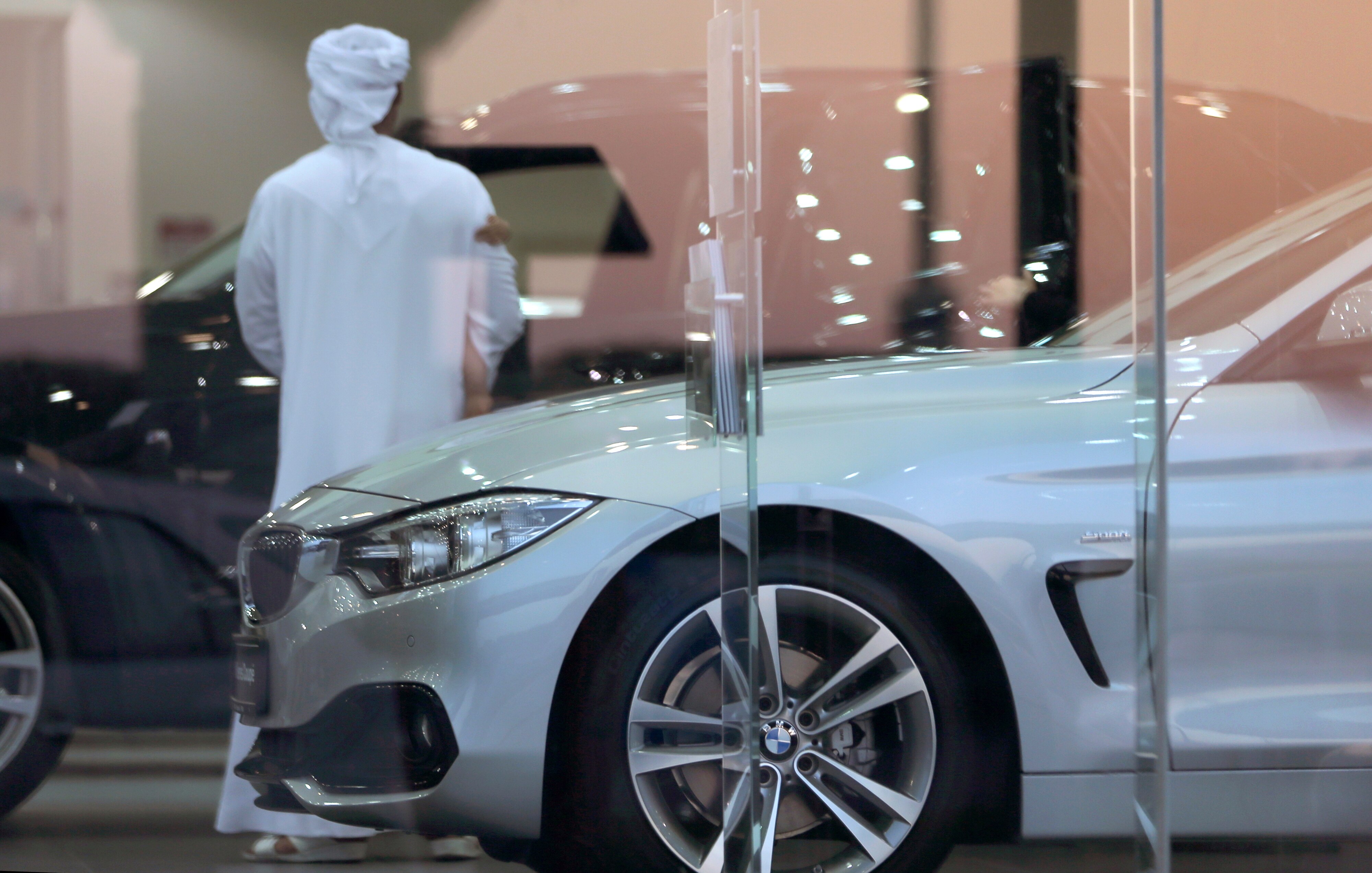 a man in a kandura stands inside a car dalership surrounded by luxury cars