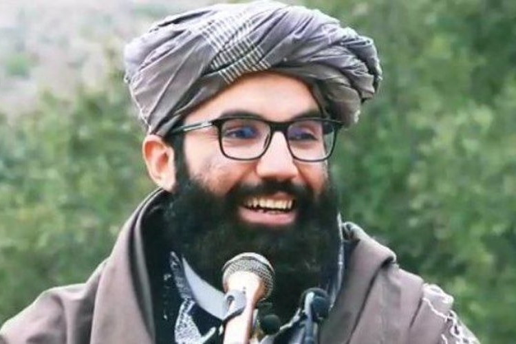 A man with a long beard wearing Afghan traditional clothing speaks into a microphone.
