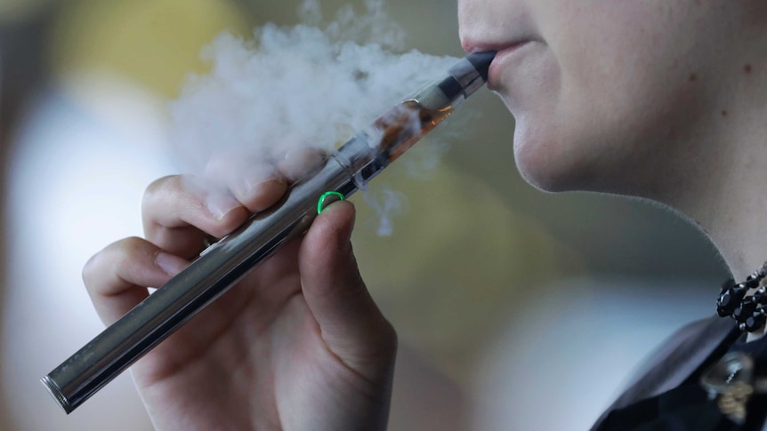 A woman exhales smoke from an e-cigarette.