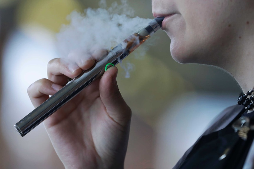 A woman exhales smoke from an e-cigarette.