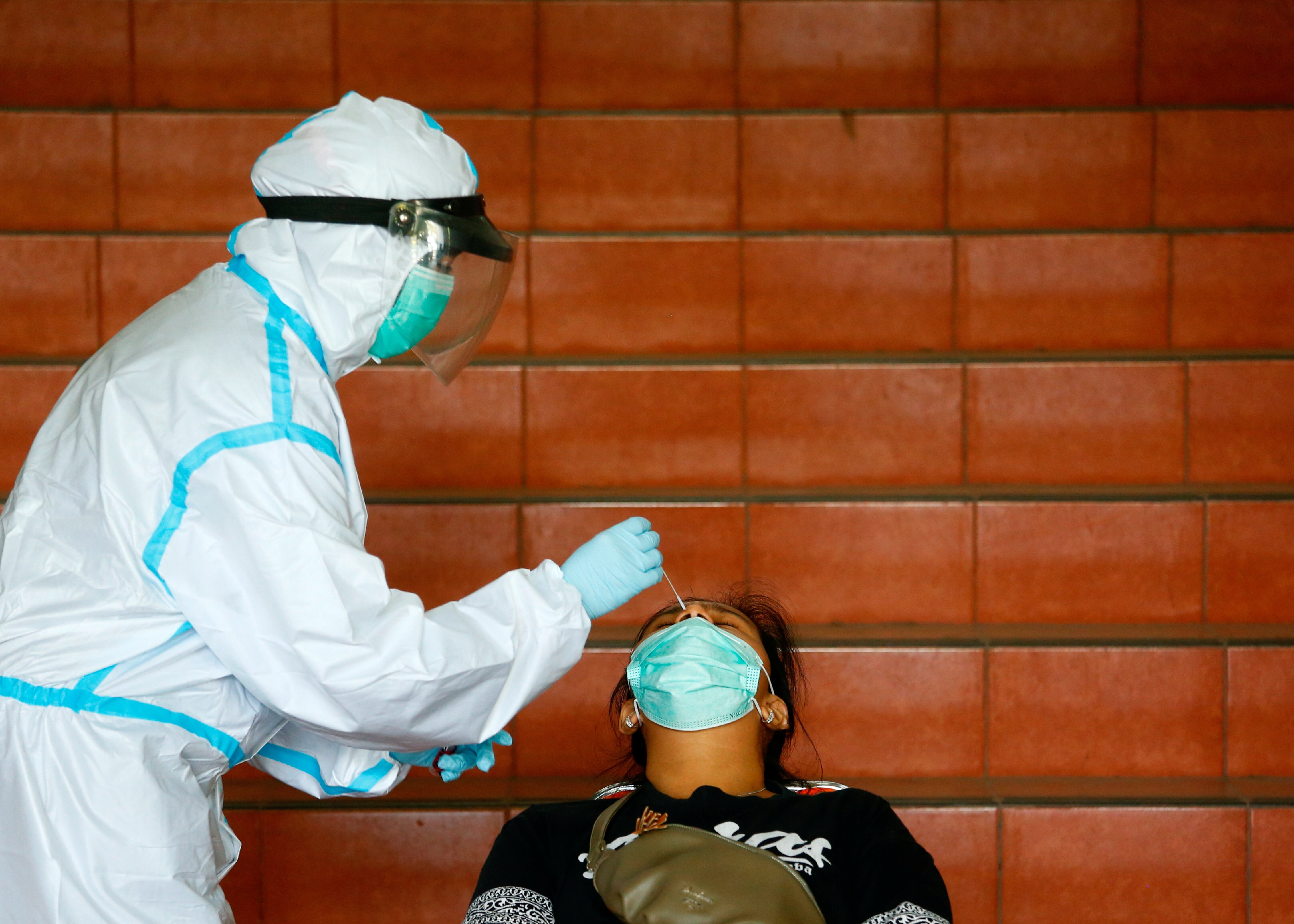 A medical worker in PPE takes a nasal swab sample from a woman
