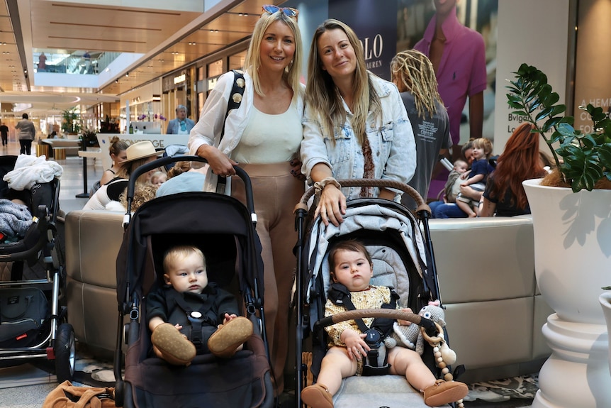 Two women and their children in prams inside a shopping centre