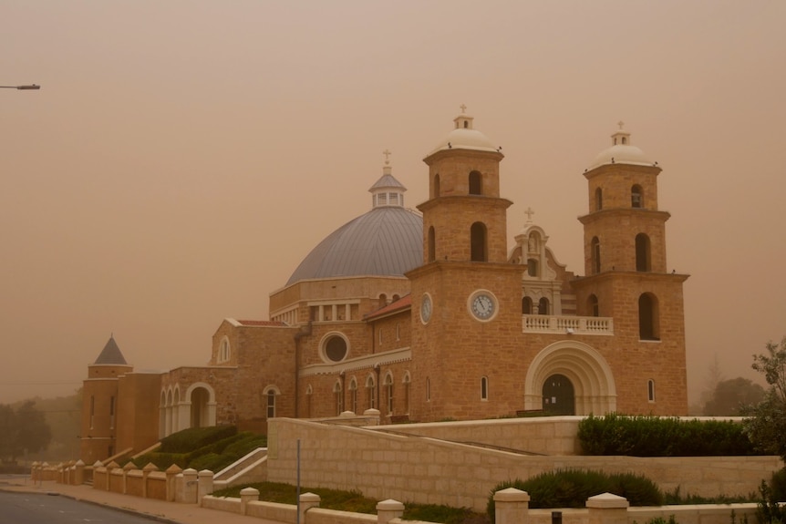 A cathedral with pale bricks, two turrets and a dome stands shrouded in dust in Geraldton.