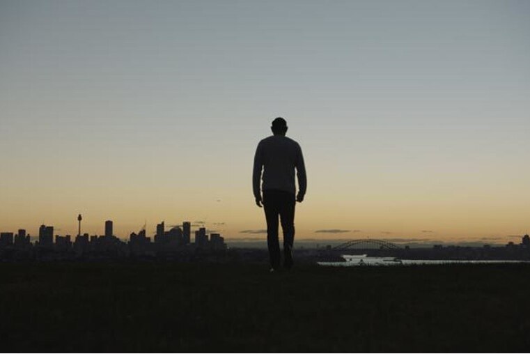A man stands silhouetted on a hilltop looking out across Sydney