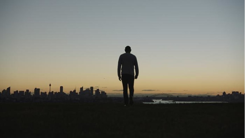 A man stands silhouetted on a hilltop looking out across Sydney