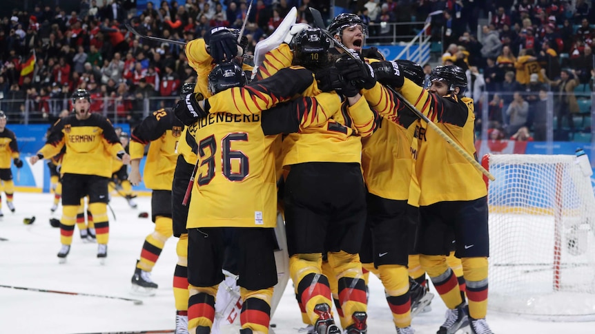 The german team shares a large group hug on the ice, celebrating their win as the crowd looks on