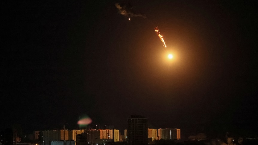 A drone explodes in a yellowish burst above the sky of Kyiv at night