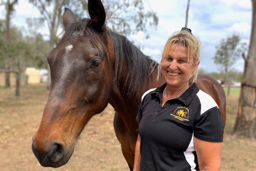 Melissa Bell smiling and standing in front of a standardbred horse in a paddock