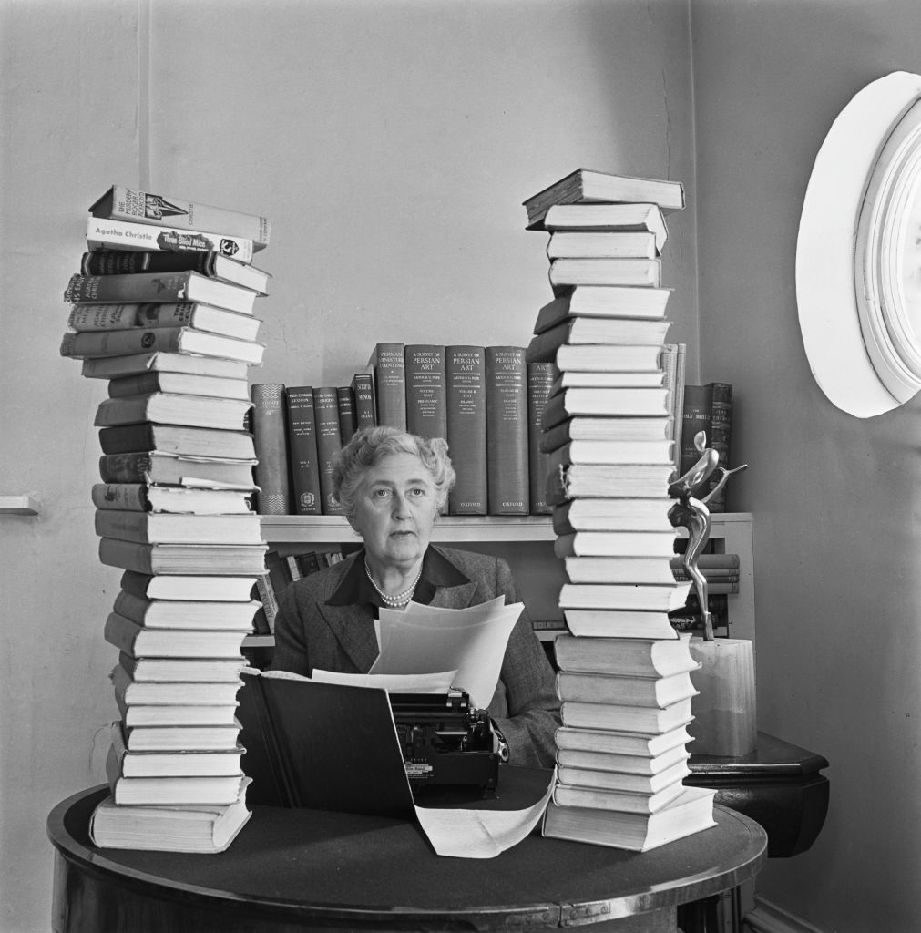 Black and white photo of older woman seated at a desk with a typewriter