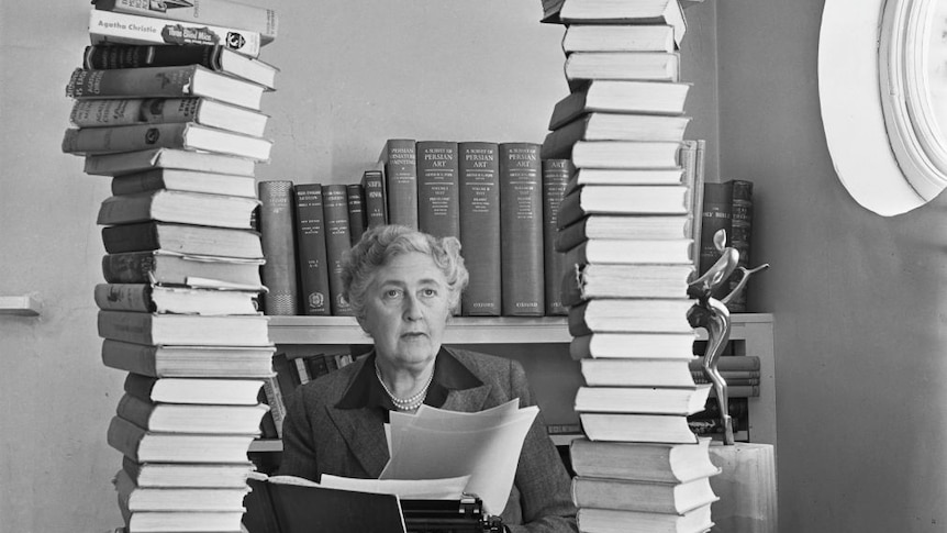 Black and white photo of older woman seated at a desk with a typewriter