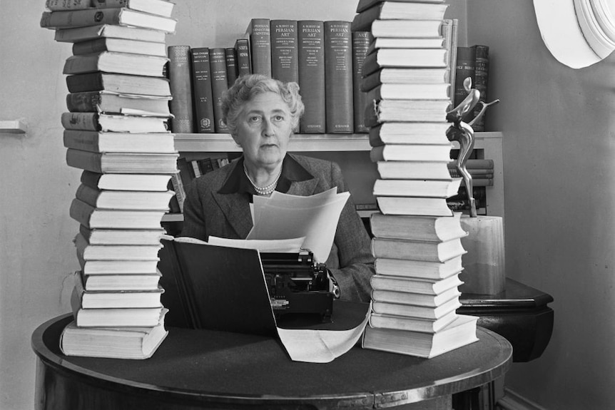 Black and white photo of older woman seated at a desk with a typewriter