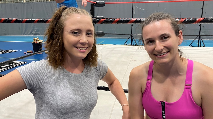 Two young women sit on the apron of a wrestling ring.