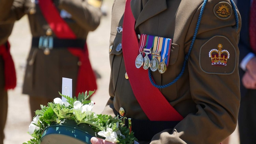 A soldier stands holding a commemorative wreath