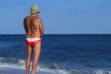 A man with a hairy back stands in the sun at the beach