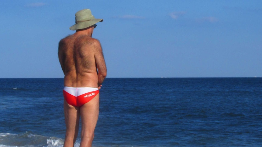 A man with a hairy back stands in the sun at the beach