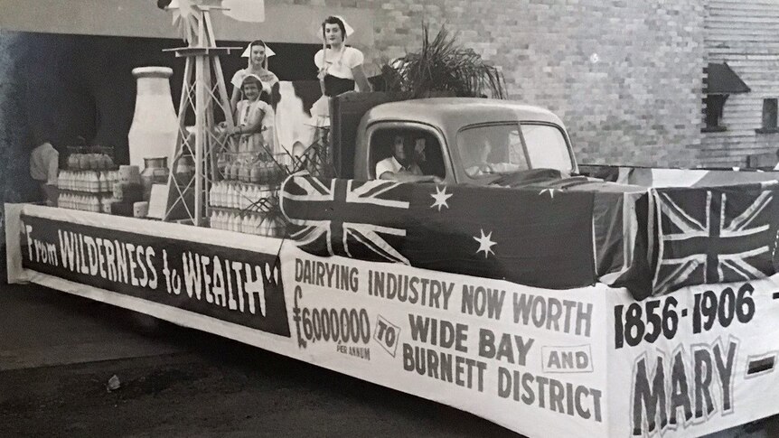 three women on a float dressed as milk maids and surrounded by milk bottles. banner reads 'from wilderness to wealth'