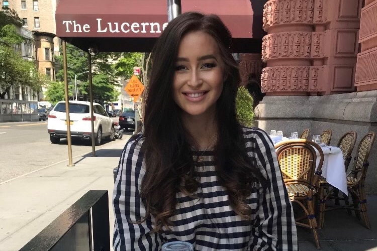 Woman with brown hair smiling, sitting outside a restaurant. 