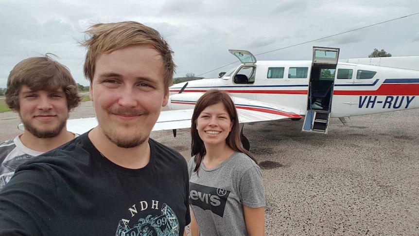 Julie Lelund, Alexander Jensen and Neikolaj Nielsen take a selfie with a plane in the background.