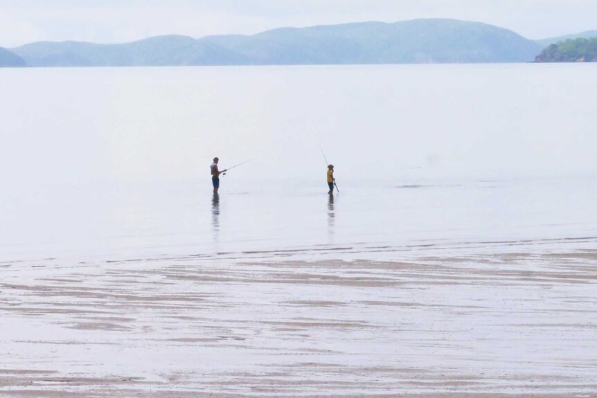 Two men fish during low tide on Palm island with islands in the background.