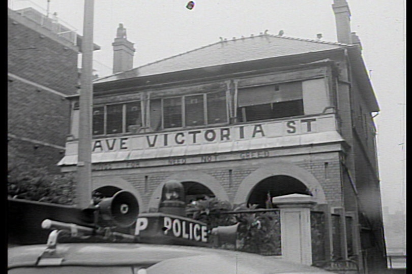 A black and white photo of a police car parked out front of a house with Save Victoria Street written on the facade.
