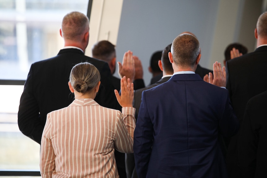 Police officers wearing formal attire are pictured from behind as they raise their hands at a swearing in ceremony
