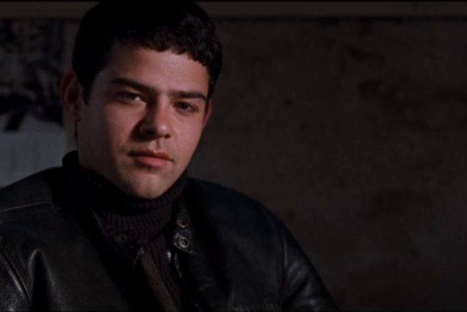 Rory Cochrane looks directly at the camera while sitting down in a black leather jacket