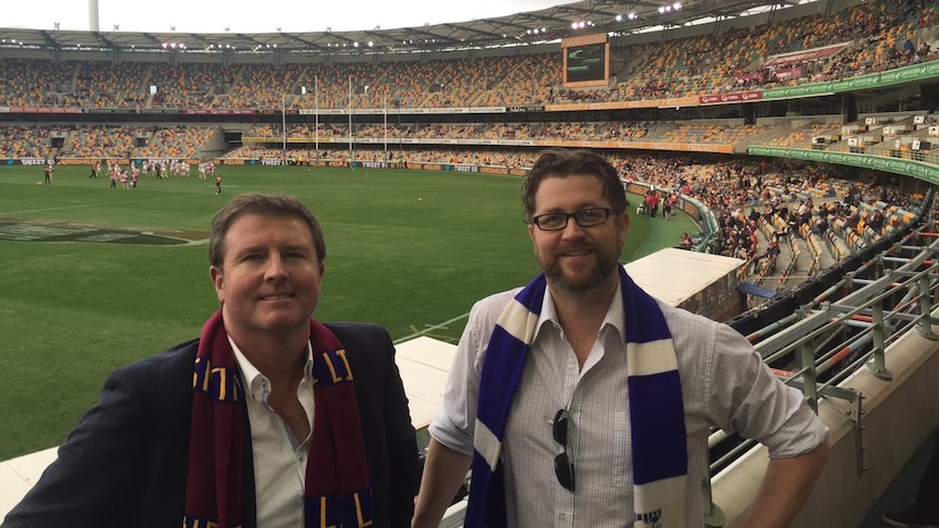 Two men stand in the crowd at a football stadium.