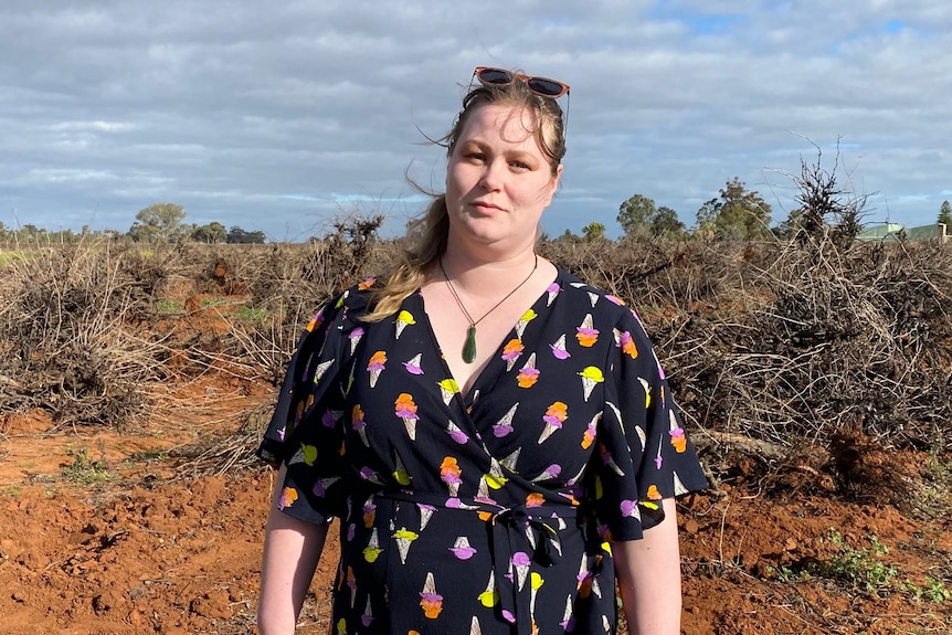 A woman wearing a black dress standing in front of rows of dead grapevines ripped out of the ground. 