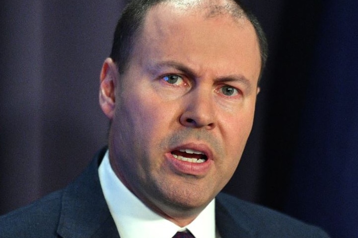 Josh Frydenberg making a speech, wearing a suit, while standing in front of an Australian flag.