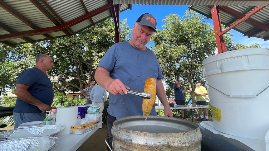 a man holds a fried fish with tongs over a barrel of oil