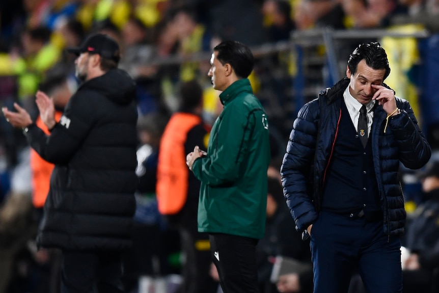 Villarreal manager Unai Emery looks down and wipes his eyes as Liverpool manager Jürgen Klopp applauds in the background.