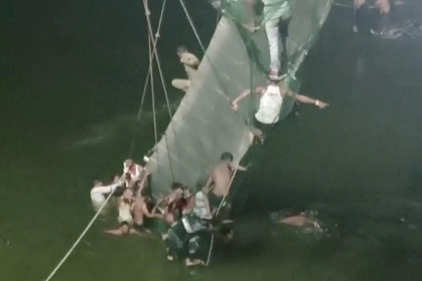 People cling on to the collapsed suspension bridge in Morbi.