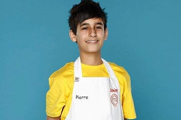 A boy wearing a chef's apron smiles at the camera