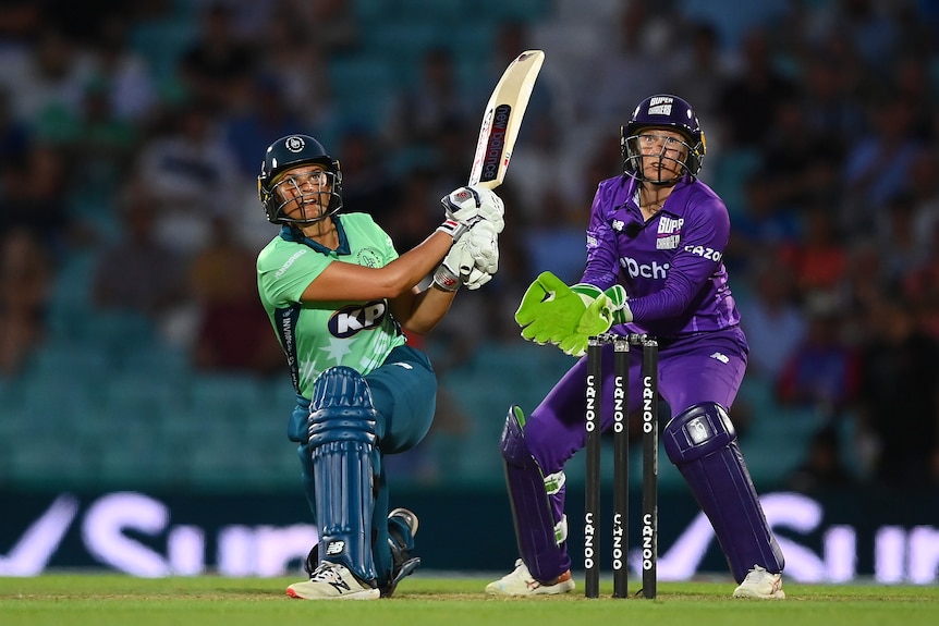 Suzie Bates plays a shot as wicketkeeper Alyssa Healy looks on during a cricket game.