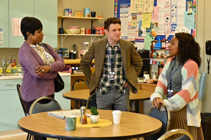 A black woman with short dark hair, white man with short brown hair and black woman with curly long hair stand in a lunch room.