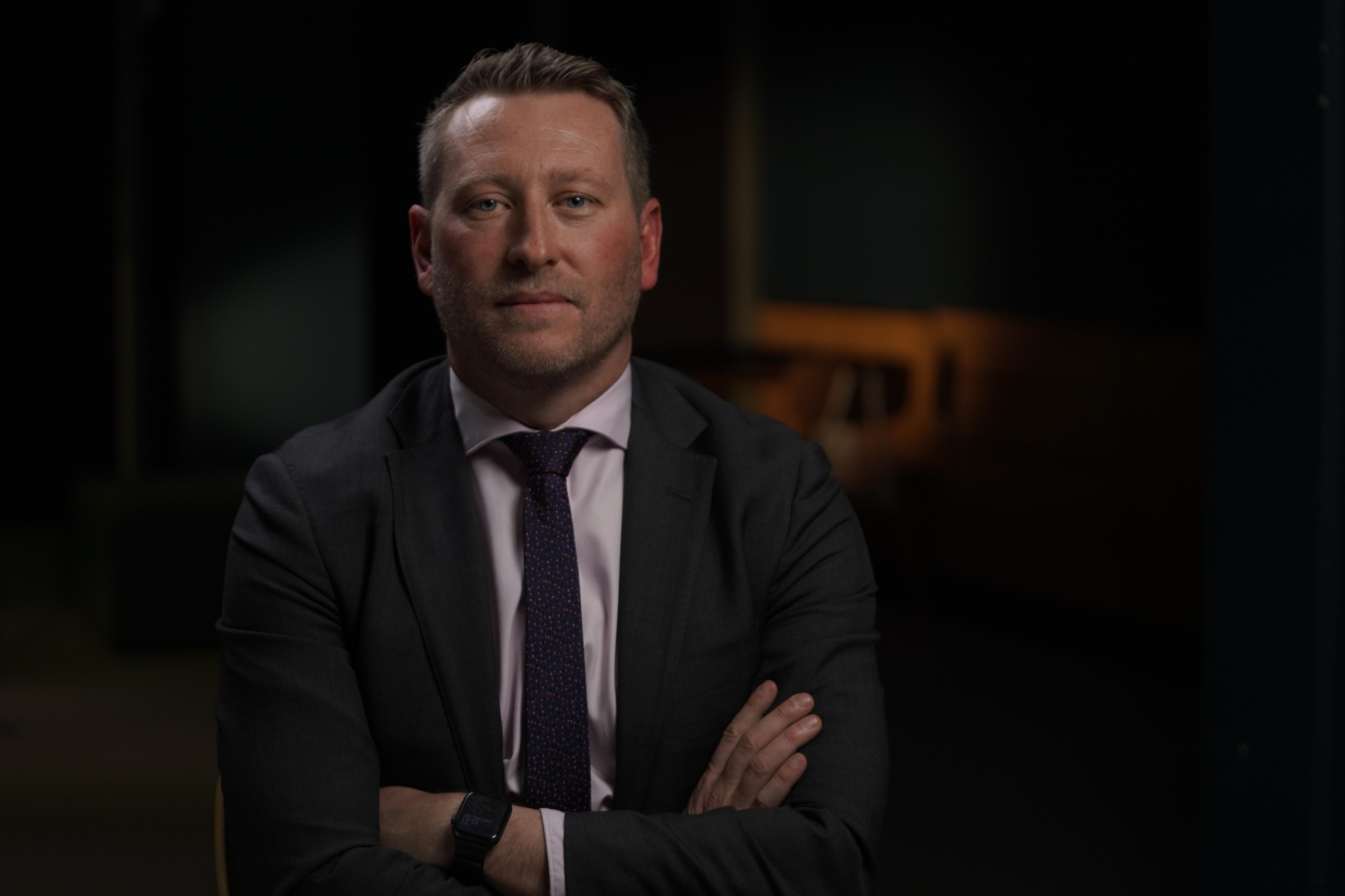 A man wearing a suit and tie has his arms crossed.