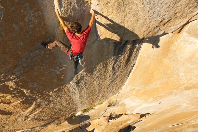 Brad Gobright in a red shirt holds on to the side of a cliff face as another climber can be seen below him