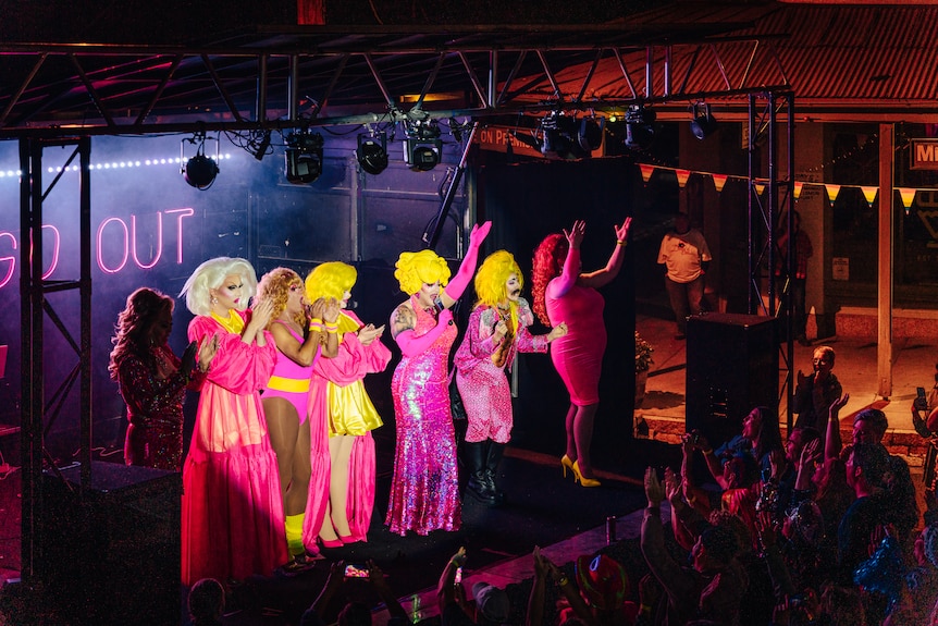 Drag queens, dressed in hot pink, dance on a stage.