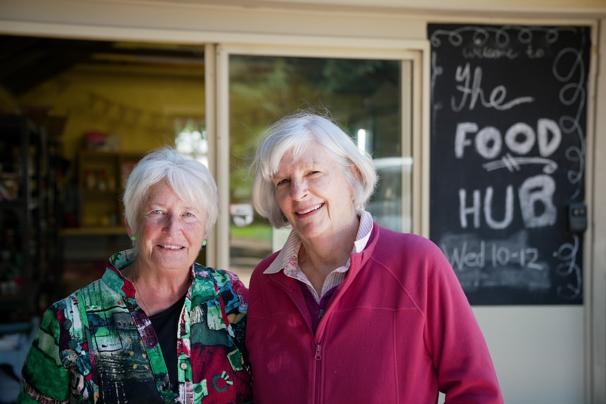 Two women stand in front of a sign that says 'The Food Hub'.