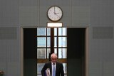 Malcolm Turnbull, frowning, walks through the House of Representatives door. A clock on the wall above his head reads 2:59.