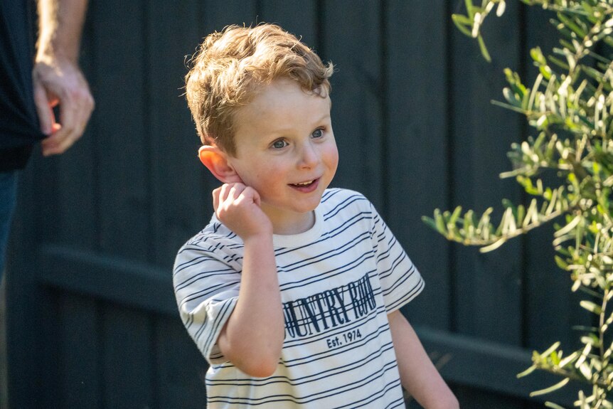 Flynn wears a white shirt with black stripes and smiles in the backyard of his home