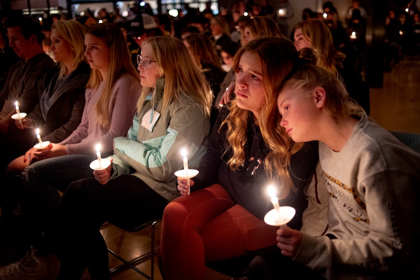 Two girls hug while holding candles.