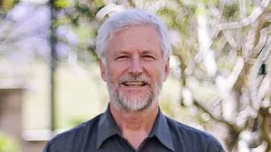 Grey-haired man with grey beard wearing black collared shirt